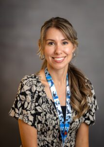 Smiling woman with long hair wearing a patterned blouse and lanyard.