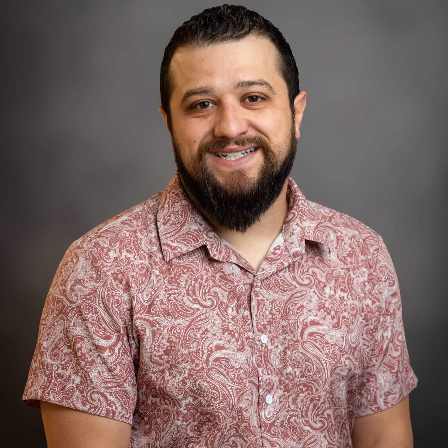 Man smiling in patterned shirt, gray background.